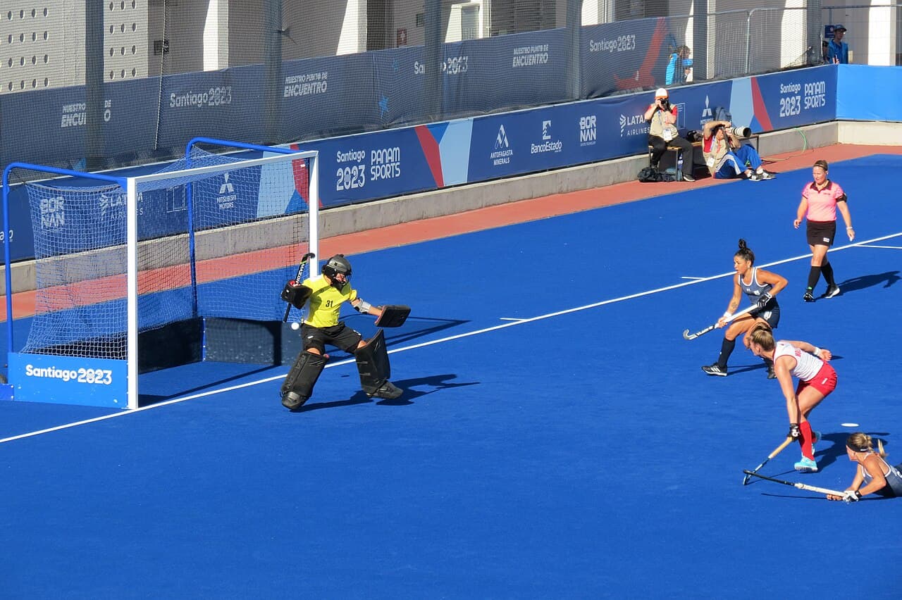 Arquera defendiendo un remate en un partido de hockey sobre césped sobre cancha azul